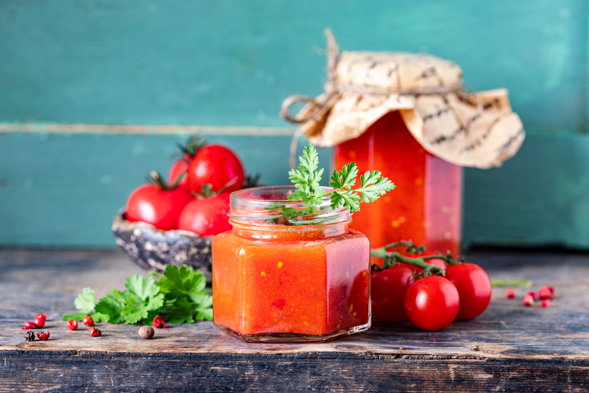 homemade tomato ketchup made from ripe red tomatoes in glass jars with ingredients on an old wooden table.